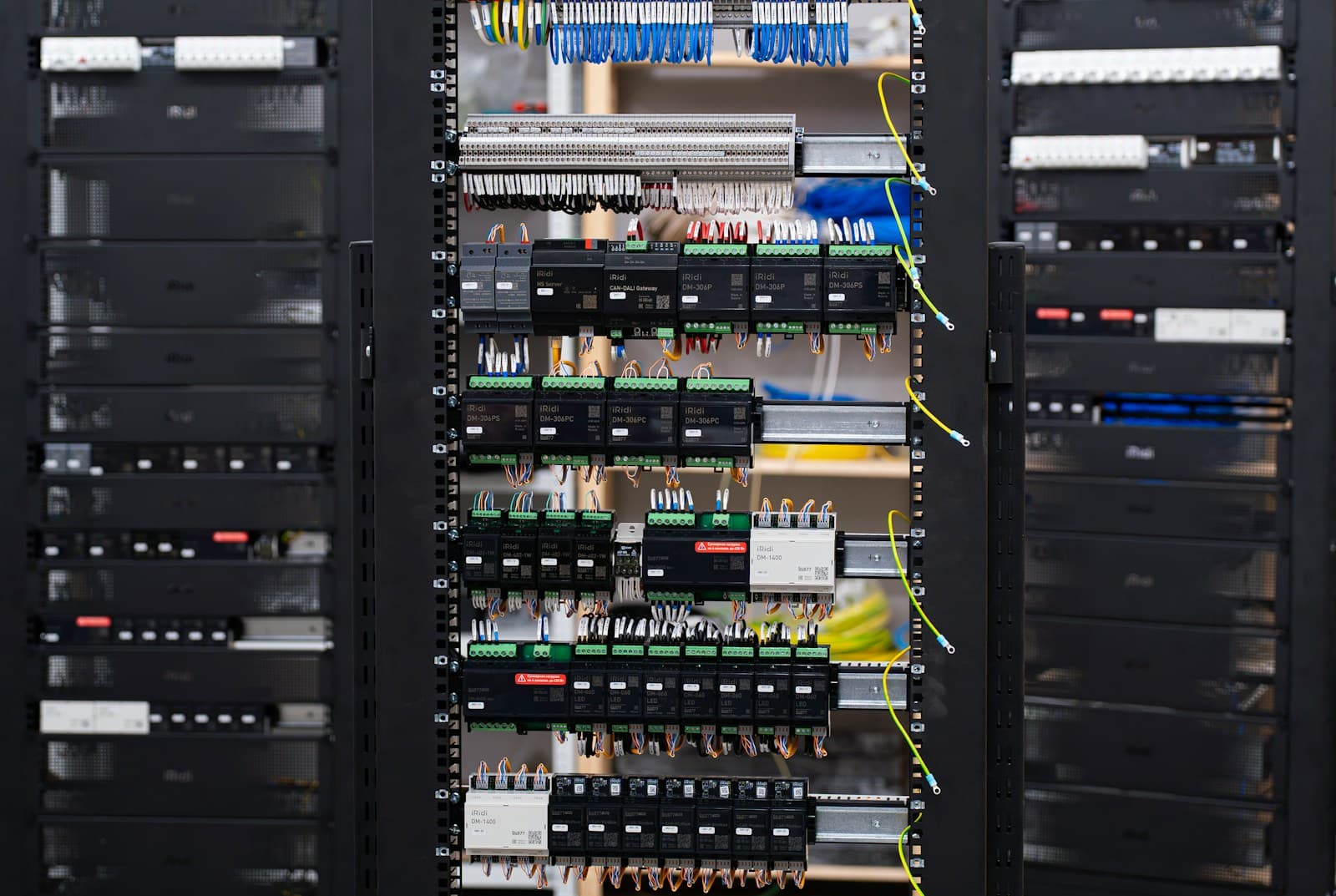 Building automation control cabinet with DIN-rail controllers and protocol gateways, rows of blue signal wires landing on terminal blocks — the typical architecture of a BMS panel that must bridge multiple protocols