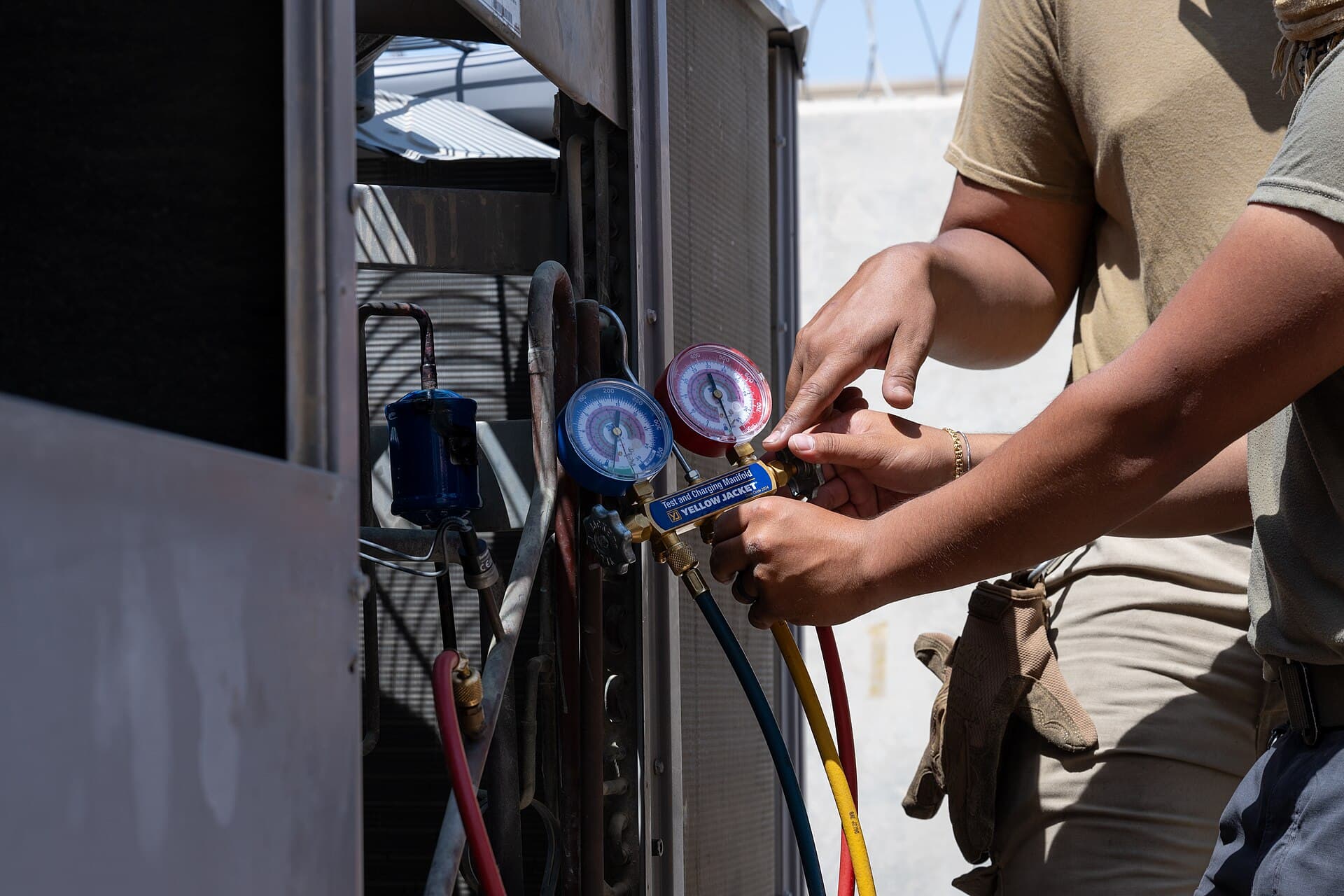 A technician reads high- and low-side pressures with a manifold gauge set on an outdoor condensing unit — field measurement is the core of functional performance testing in the commissioning process