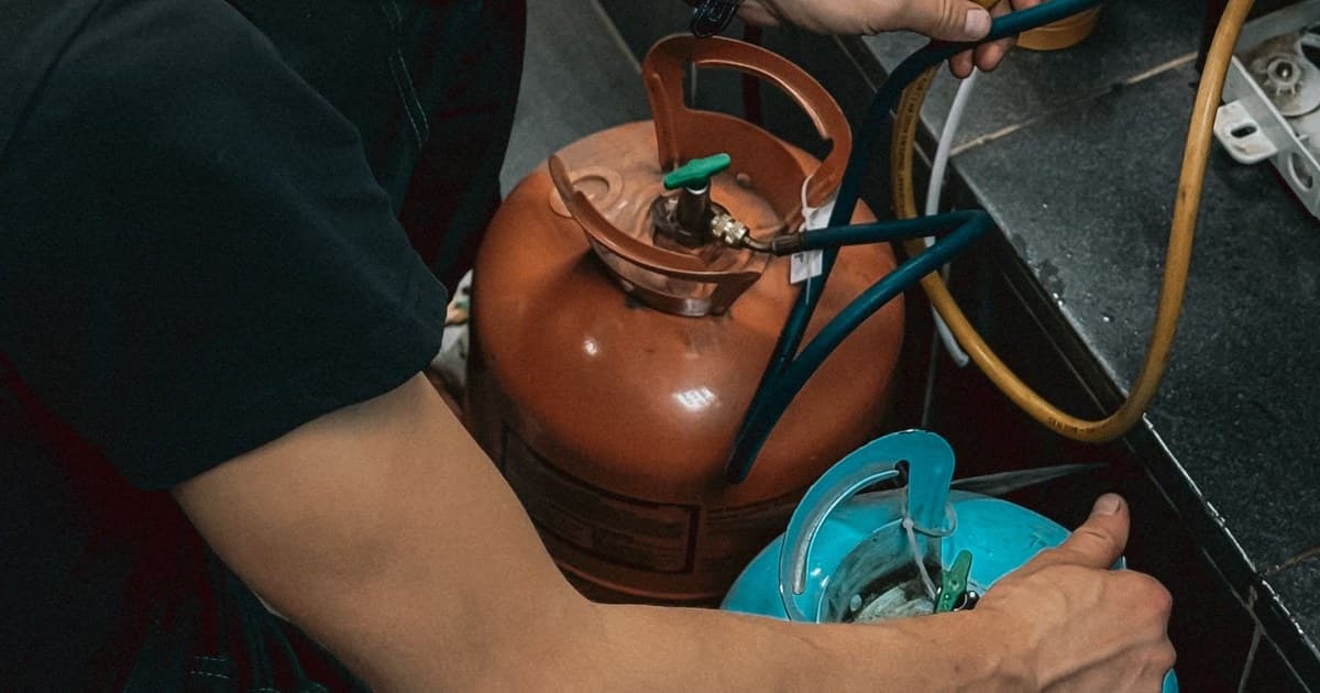Technician charging refrigerant from a cylinder through a manifold gauge set during a refrigerant and oil changeover